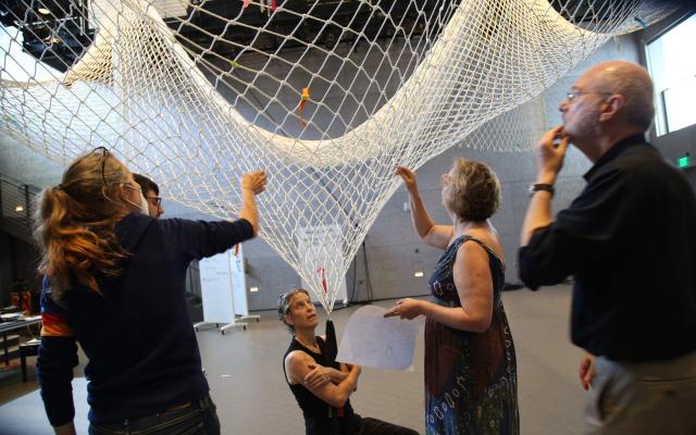Five people hold different sections of a large net